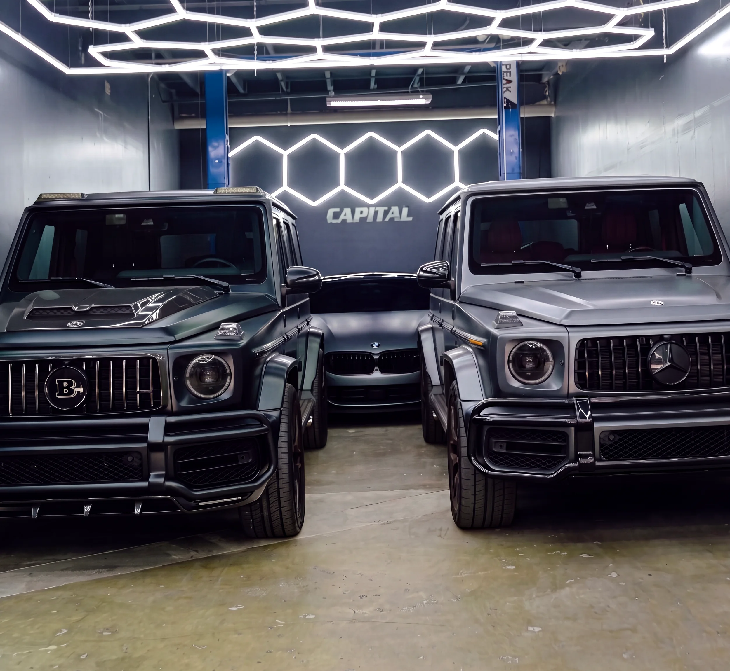 Two Mercedes G-Wagons inside the Capital Collision Center shop under hexagon lights